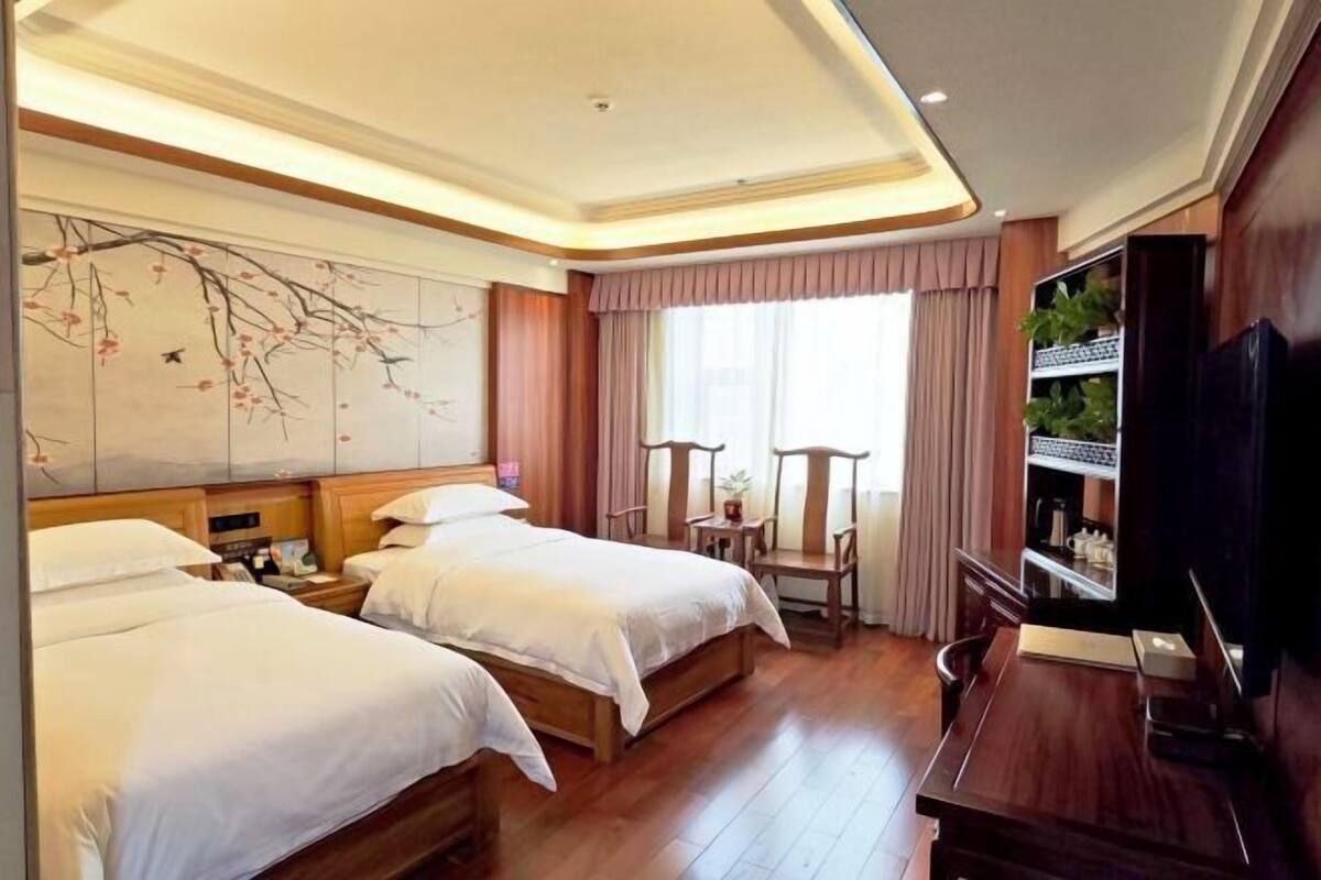 A hotel room with two beds, a large wall mural, a television, and a wooden desk.
