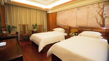 A hotel room with two beds, a desk, a chair, and a wall with a tree mural.