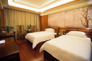A hotel room with two beds, a desk, a chair, and a wall with a tree mural. - Wenhe Hotel (Hepu)