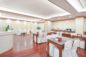 Un salón de conferencias de hotel con mesas redondas, sillas blancas y un mostrador de recepción.