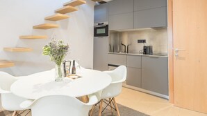 A modern kitchen with grey cabinets, a built-in oven, and a stainless steel countertop. There is a dining table with white chairs and a vase with flowers. - Lovely apartment with big private terrace in Sant Gervasy for monthly rentals (Barcelona)