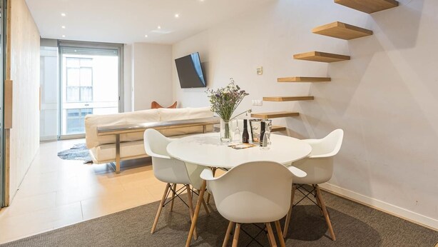 A modern living room with a dining area, a sofa, a TV, and built-in wooden shelves. - Lovely apartment with big private terrace in Sant Gervasy for monthly rentals (Barcelona)