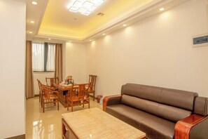 Quarto de hotel com sofá, mesa de jantar com cadeiras e pequena mesa com abajur.