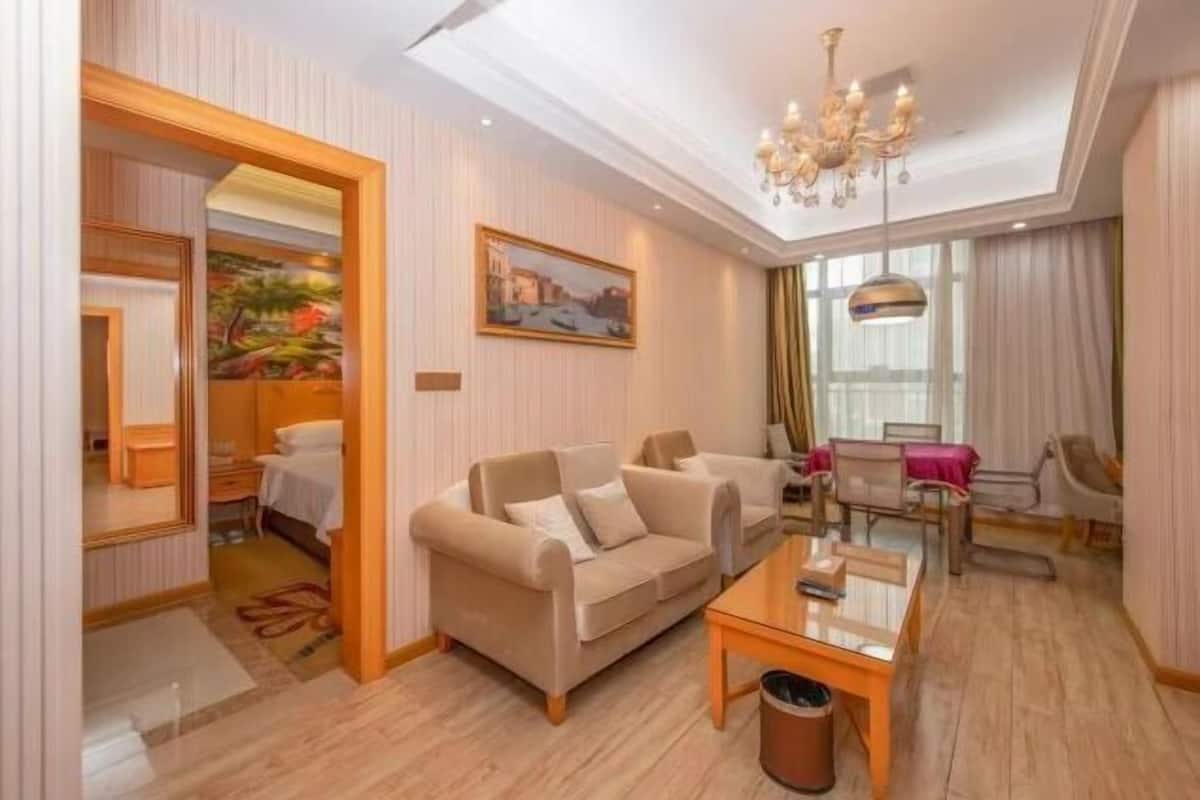 A hotel room with a sofa, a dining table, a chandelier, and a painting on the wall.