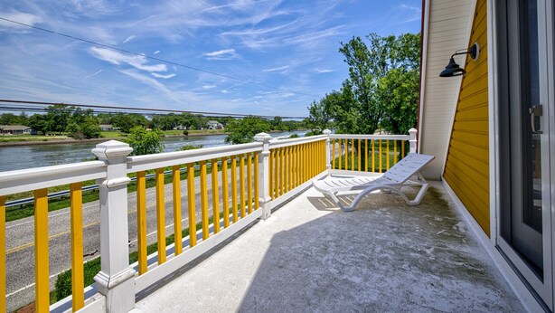 Un balcon doté d’une balustrade blanche et de touches de couleur jaune, qui offre une vue sur une rivière et un pont situé au loin.