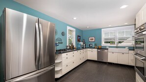 Une cuisine moderne dotée d’un réfrigérateur en acier inoxydable, de meubles blancs, d’une cuisinière à gaz et d’une fenêtre avec des stores.