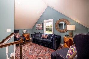 Une pièce chaleureuse avec un canapé bleu foncé, un tapis à motifs et un miroir rond accroché au mur.