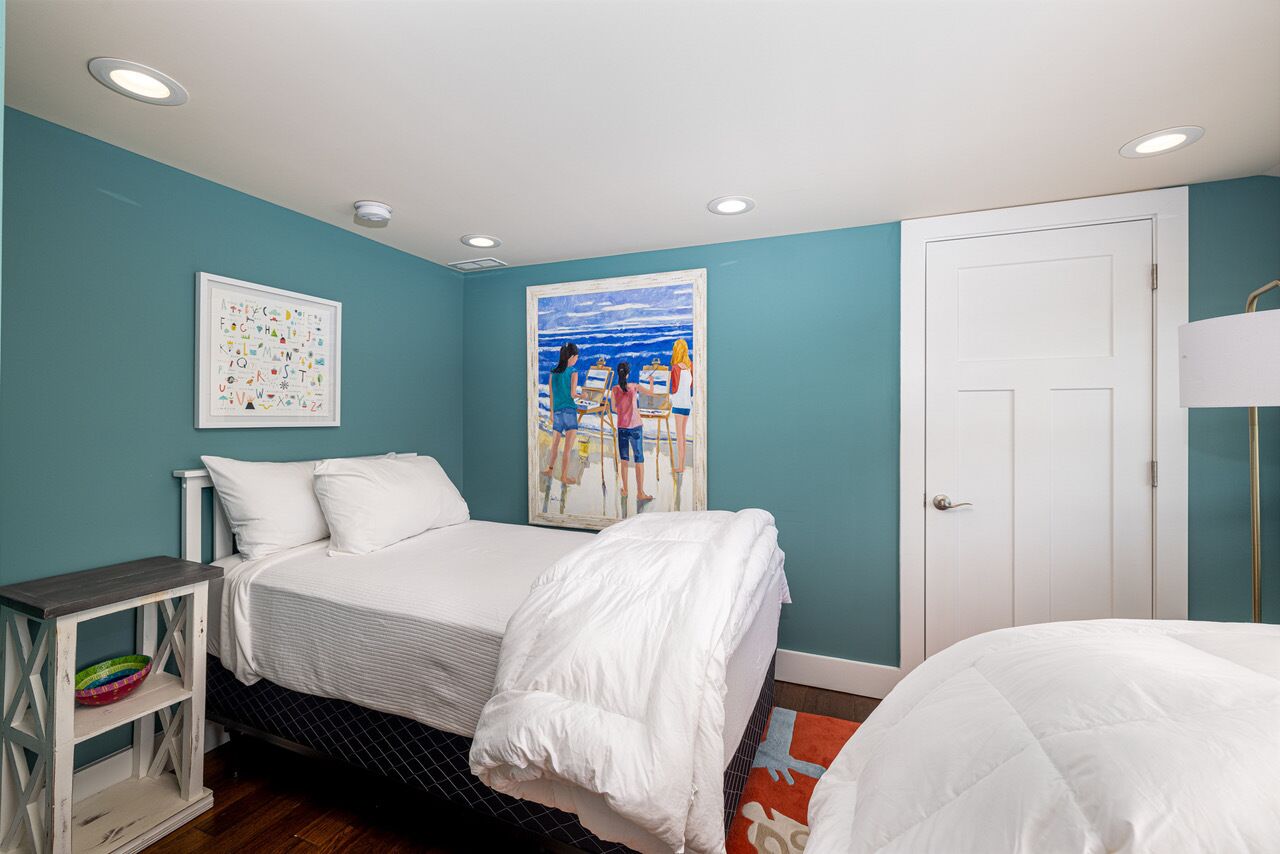 A bedroom with a bed, a painting, a door, and a small table.