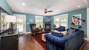 Un salon avec un canapé bleu, deux fauteuils, un ventilateur de plafond et un tapis rouge.