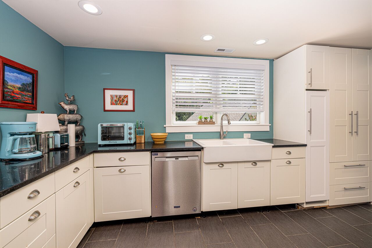 A kitchen with white cabinets, a dishwasher, a sink, and a window with blinds.