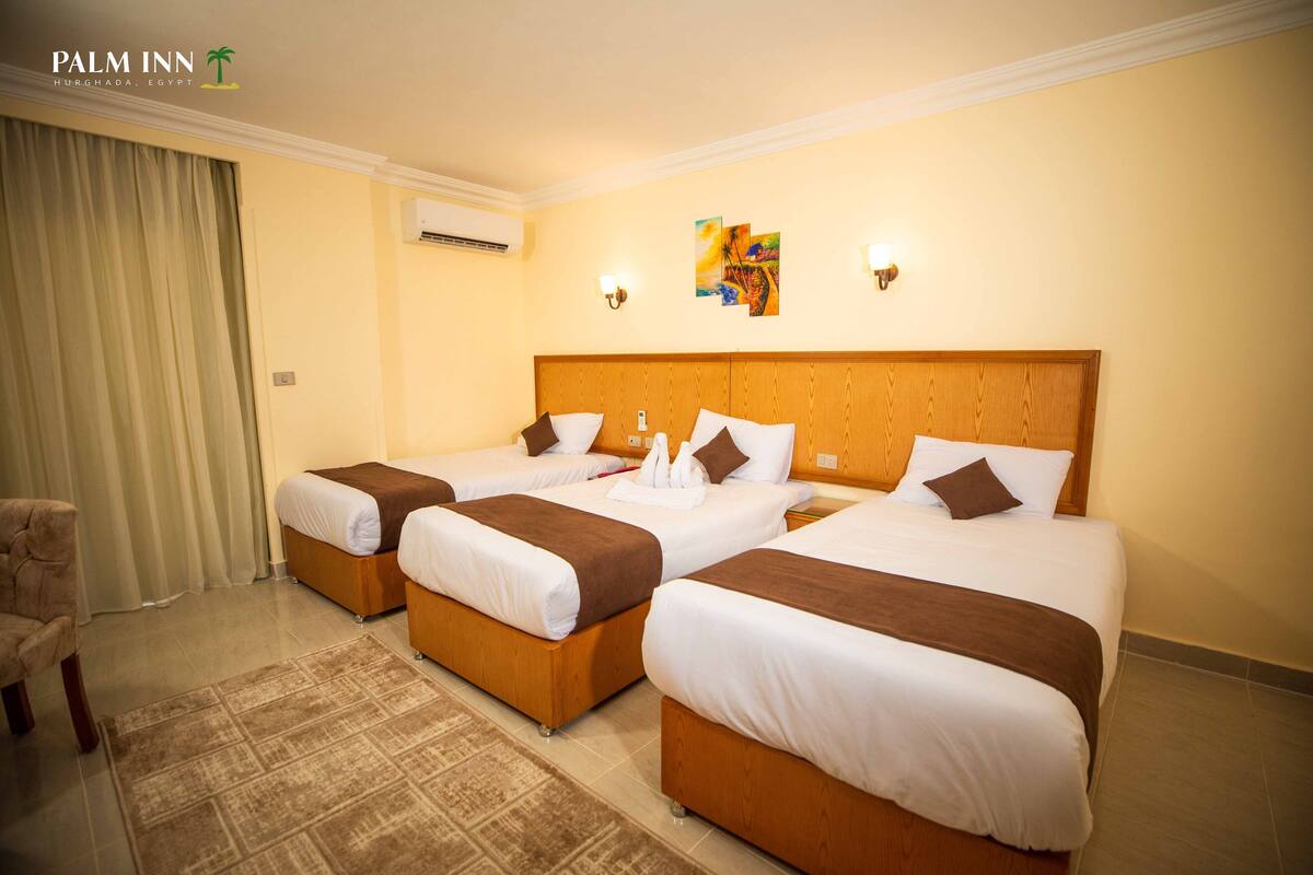 A hotel room with three beds, a chair, and a decorative wall piece.