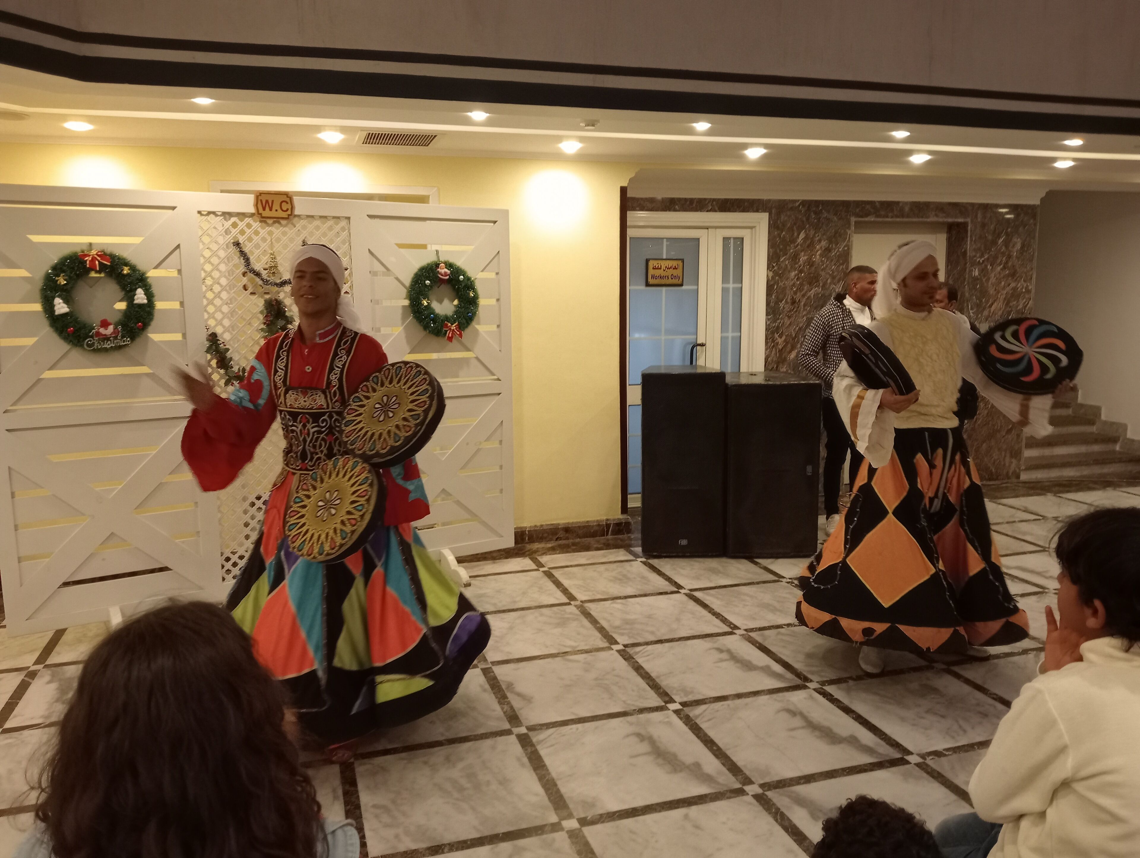 Un evento festivo con artistas vestidos con trajes tradicionales, un letrero que dice 'Solo Personal' y un adorno navideño.