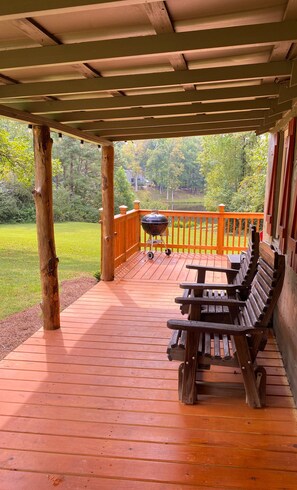 A wooden deck with a covered area, a grill, and a row of benches.