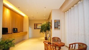 A hotel lobby with a reception desk, a potted plant, and two wooden chairs around a small table. - Super 8 Hotel (Shucheng Chunqiu South Road Cimugong) (Shucheng)