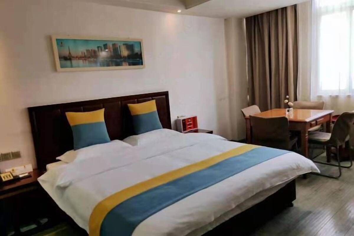 Hotelkamer met een groot bed, een bureau en een stoel. Er hangt een schilderij aan de muur en er is een raam met gordijnen.