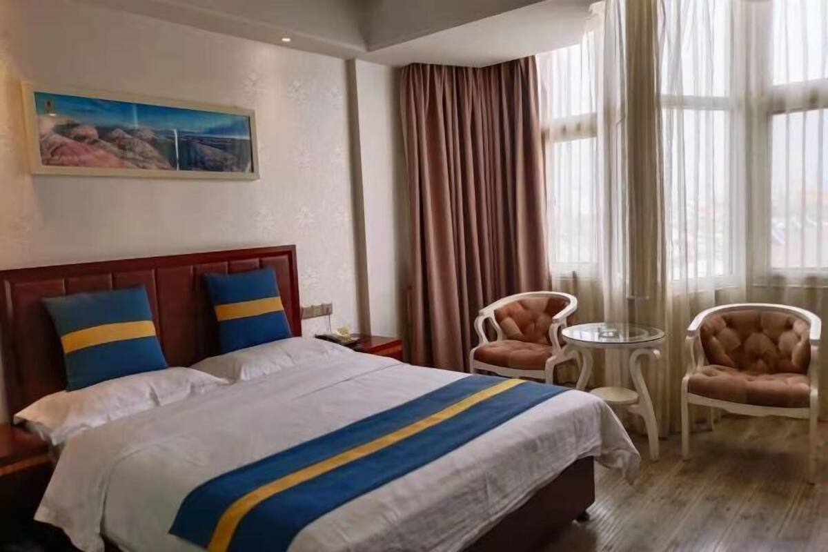 Een hotelkamer met een groot bed, twee stoelen, een klein tafeltje en een schilderij aan de muur.