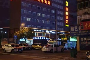 Un hotel de varios pisos, con letreros iluminados y coches aparcados en la entrada.