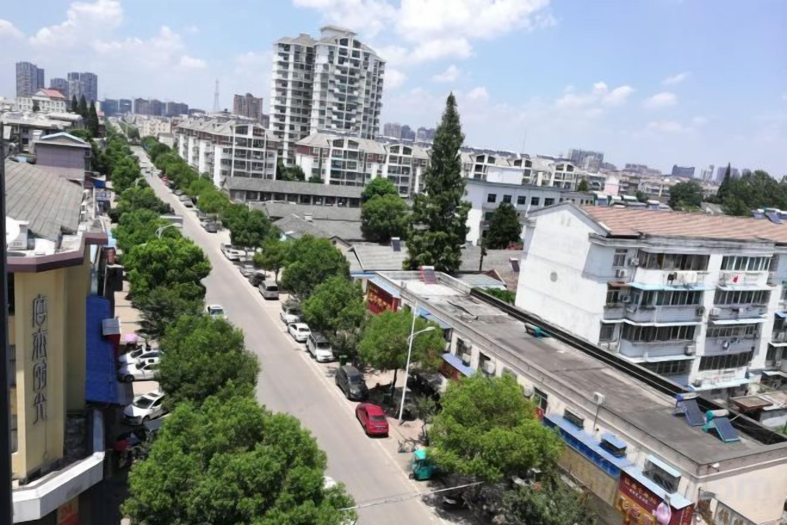 A city street with buildings, trees, and parked cars.