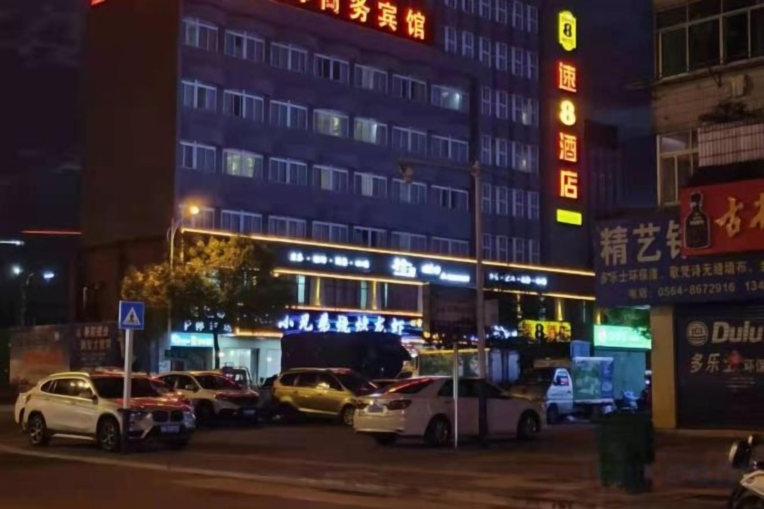 A multi-story hotel with illuminated signage, a parking lot with several cars, and a visible entrance.