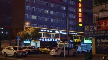 A multi-story hotel with illuminated signage, a parking lot with several cars, and a visible entrance.