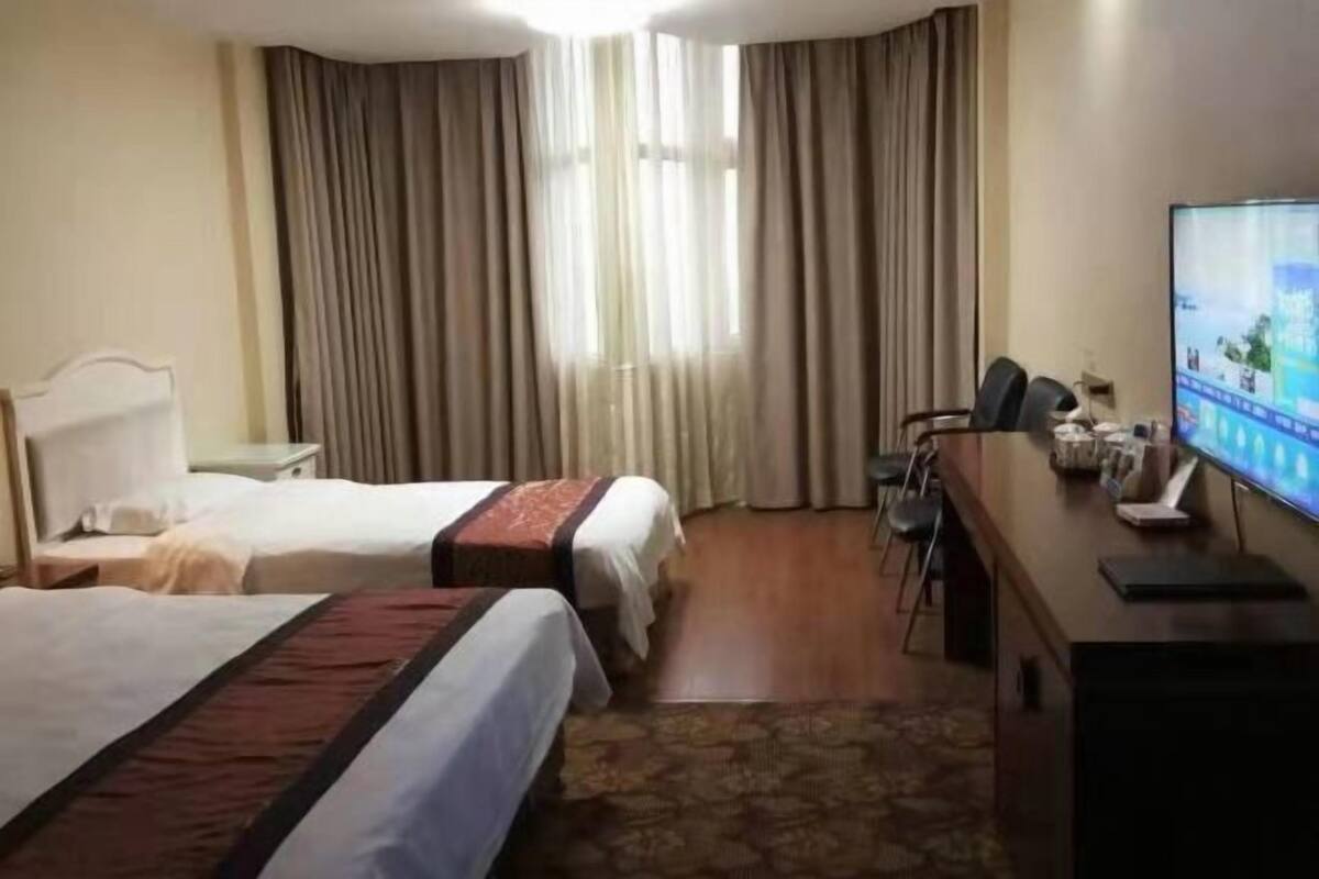 Hotelkamer met twee bedden, een bureau met een computer, een televisie en een raam met gordijnen.