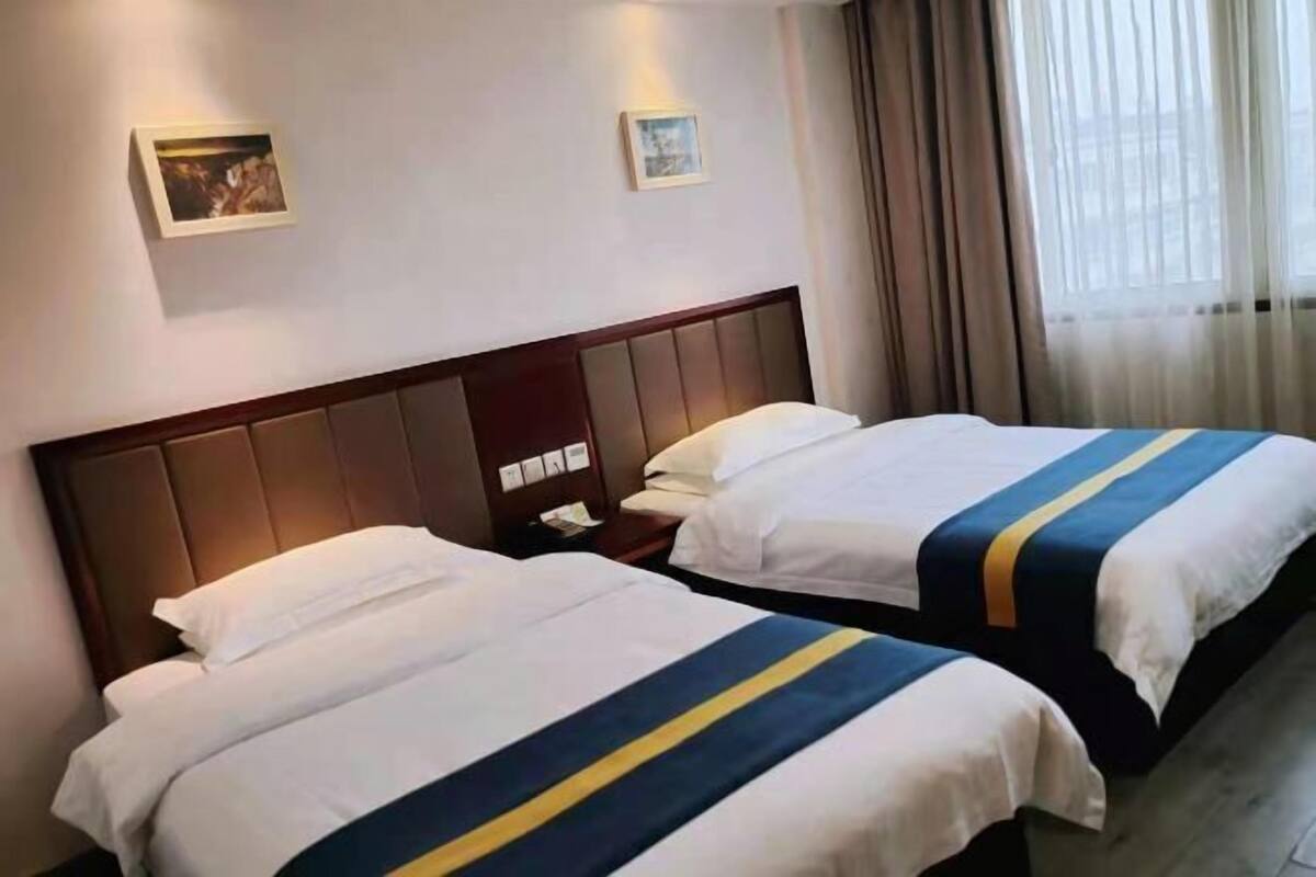 Twee bedden met witte lakens en een geleerd en blauw gestreept dekbed, een houten hoofdbord, en een nachtkastje met een telefoon en een lamp.