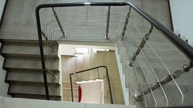 Un escalier avec des rampes et une main courante en métal, menant à une pièce dotée d’une porte blanche et d’un objet rouge posé sur le sol.
