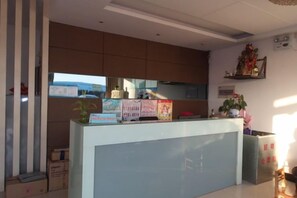 A reception desk with a glass partition, a plant, and informational posters. - Haitian Hotel (Wuhu)