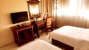 Une chambre d’hôtel équipée d’une télévision, d’un bureau avec une chaise, de deux lits et d’une fenêtre avec des rideaux.