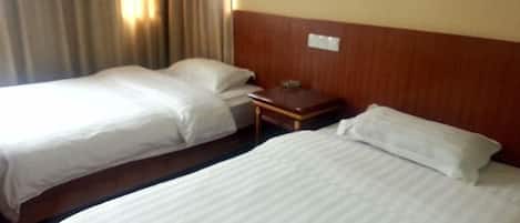 Habitación de hotel con dos camas individuales, cabecera de madera, mesita de noche y ventana con cortinas.