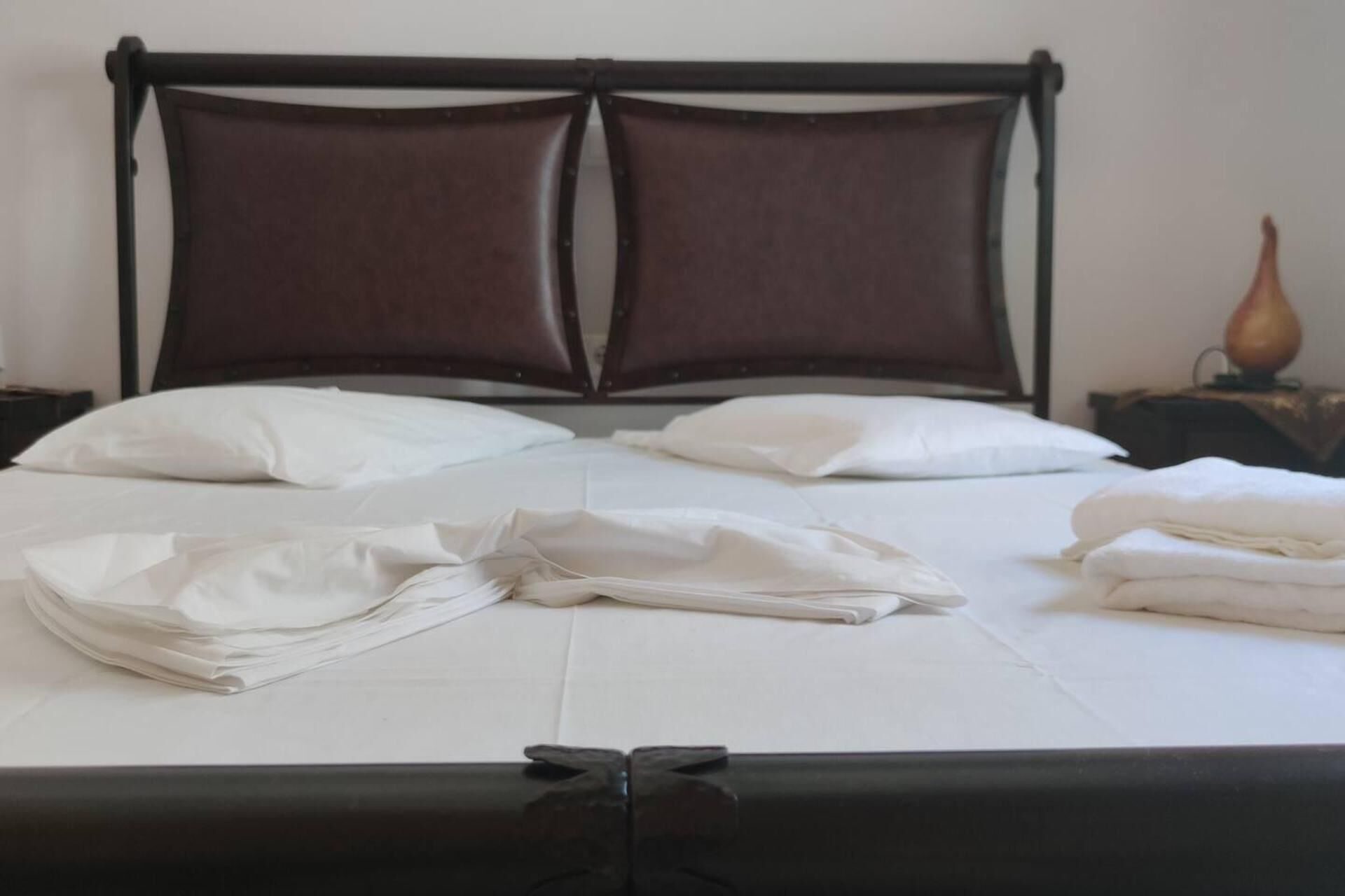 A neatly made bed with white linens and pillows, a dark wooden headboard, and a small table with a vase.