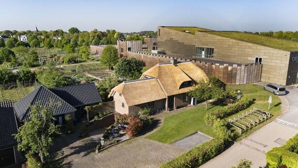A modern building with a unique thatched roof structure, surrounded by well-maintained gardens and a parking area.