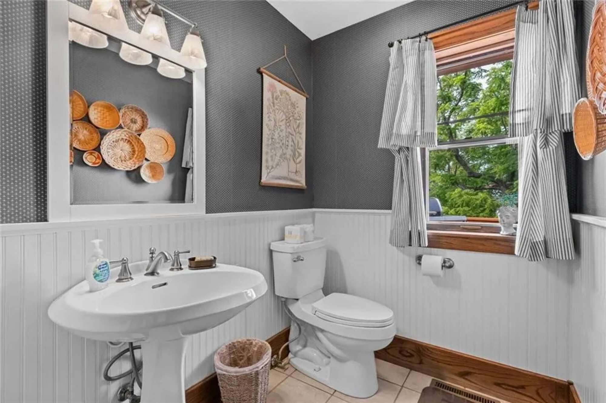 Een badkamer met een wit wastafel, toilet en een raam met gordijnen.