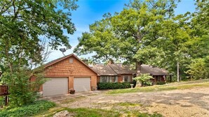 A two-story house with a garage, surrounded by trees and a grassy yard. - White River Mountain Manor- Million dollar view (Eureka Springs)
