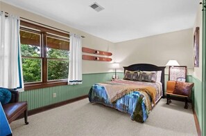 A bedroom with a large bed, two bedside tables, a window with curtains, and a view of greenery outside.