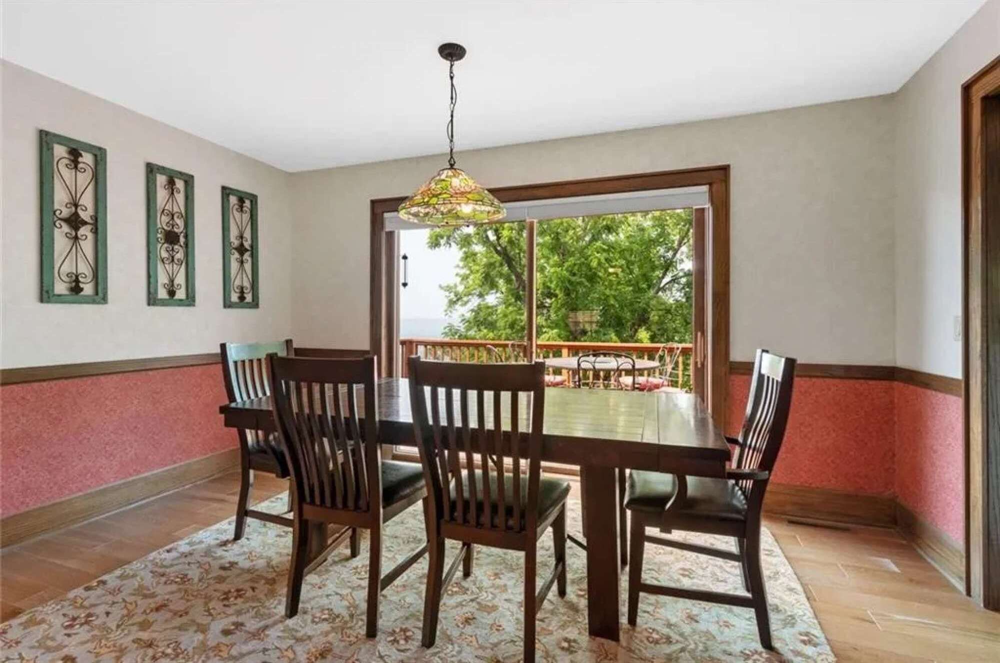 Un espace repas avec une table et des chaises en bois, un luminaire suspendu et une vue sur l’extérieur grâce à une grande fenêtre.