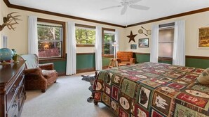 A bedroom with a quilted bedspread, a ceiling fan, a dresser, a chair, and windows with curtains. - White River Mountain Manor- Million dollar view (Eureka Springs)