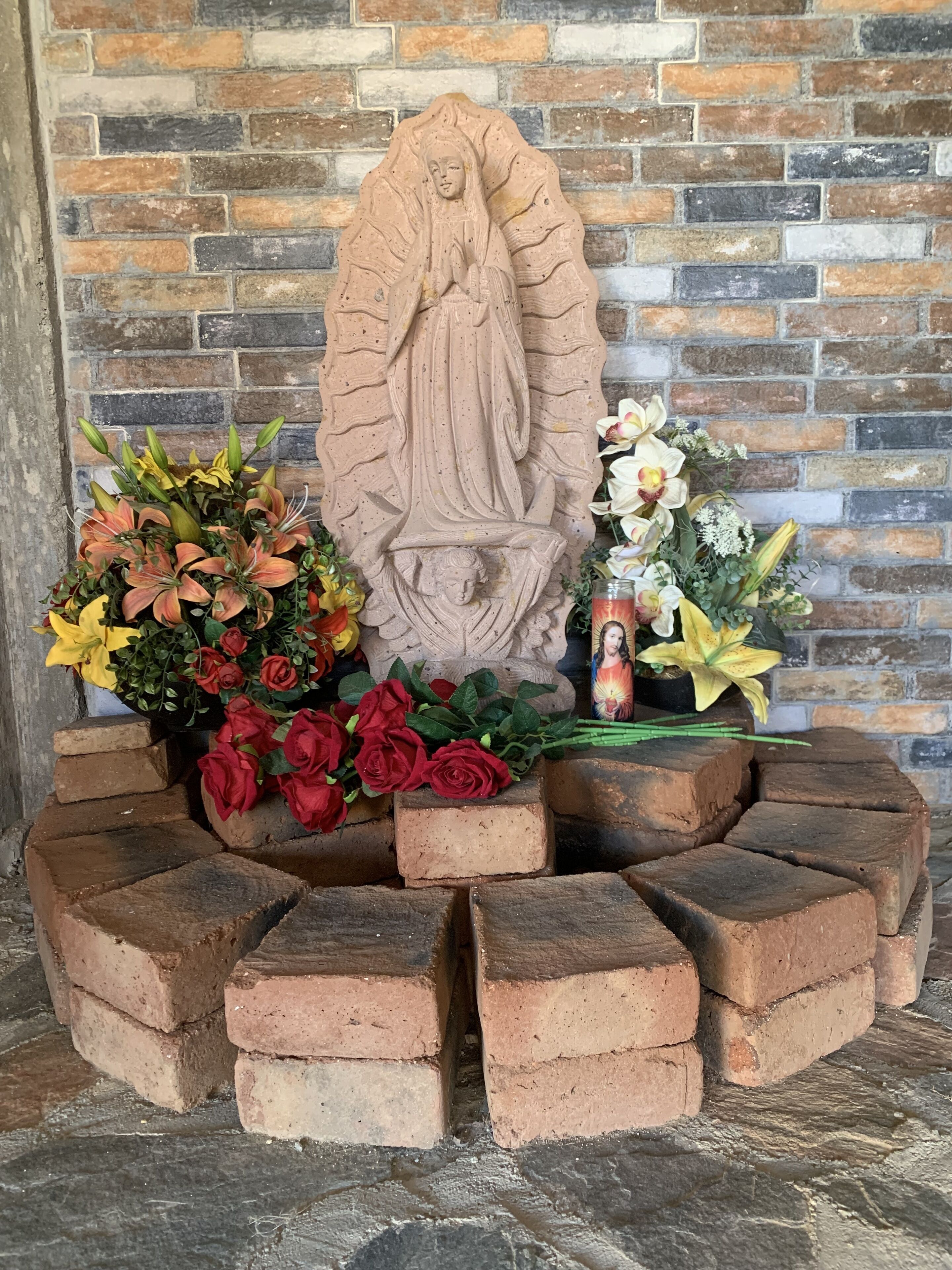Un altar de ladrillo con una estatua, rodeado de flores y velas.
