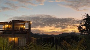 A rustic cabin with a balcony, surrounded by lush greenery and mountains in the background. - Cerritos Baja Eco Pet Friendly Boutique stay (El Pescadero)