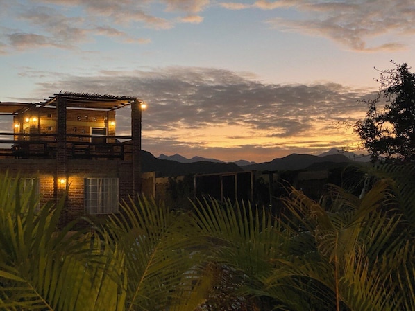 A rustic cabin with a balcony, surrounded by lush greenery and mountains in the background. - Cerritos Baja Eco friendly Boutique stay (El Pescadero)
