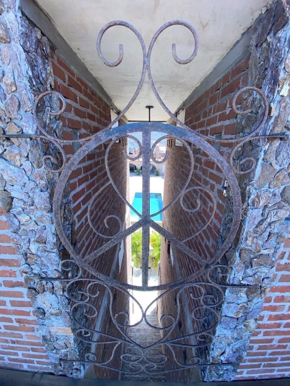 A wrought iron gate with a circular design, set in a stone wall with a brick pattern.