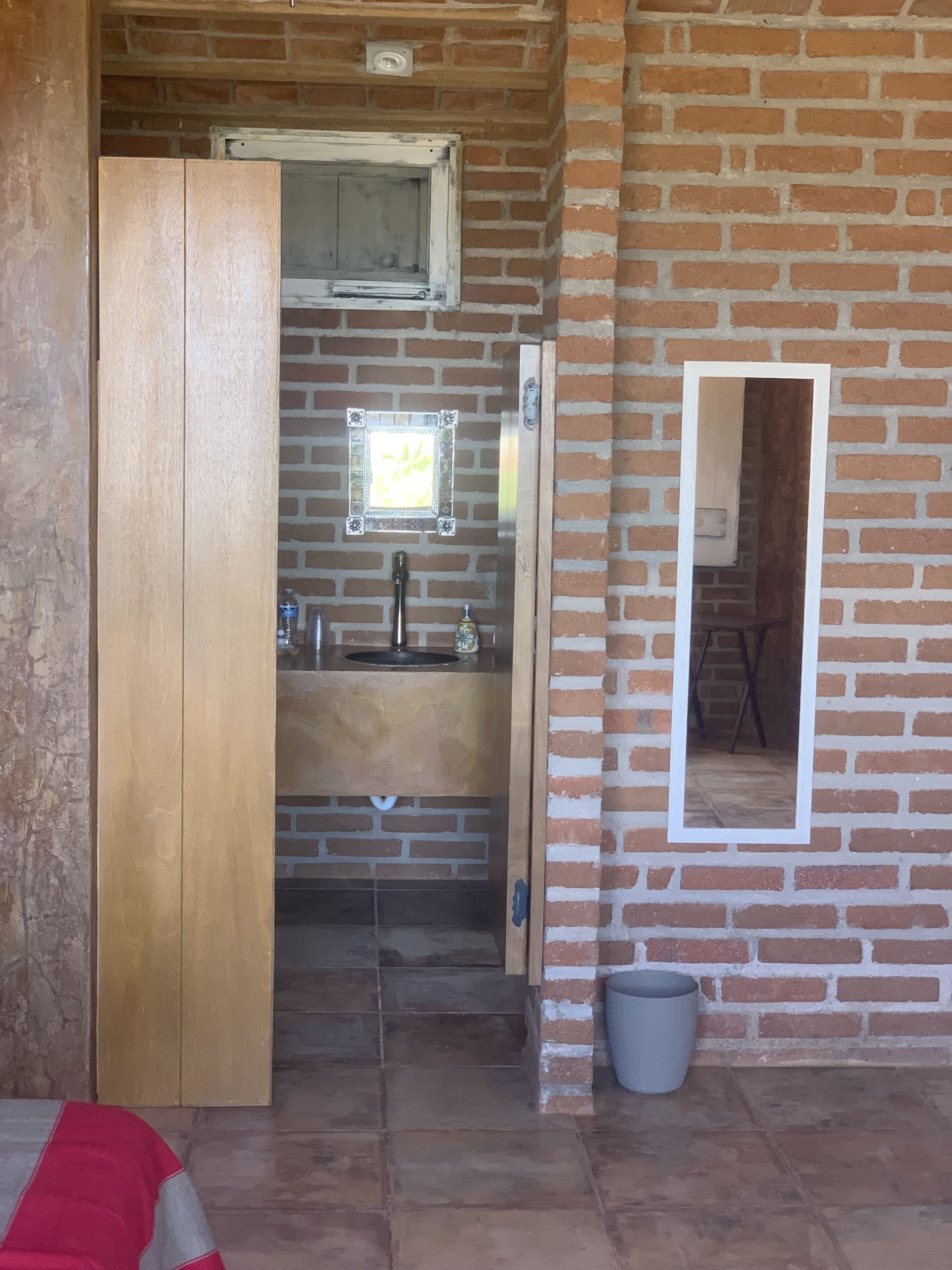 A bathroom with a wooden door, a sink, a mirror, and a window.