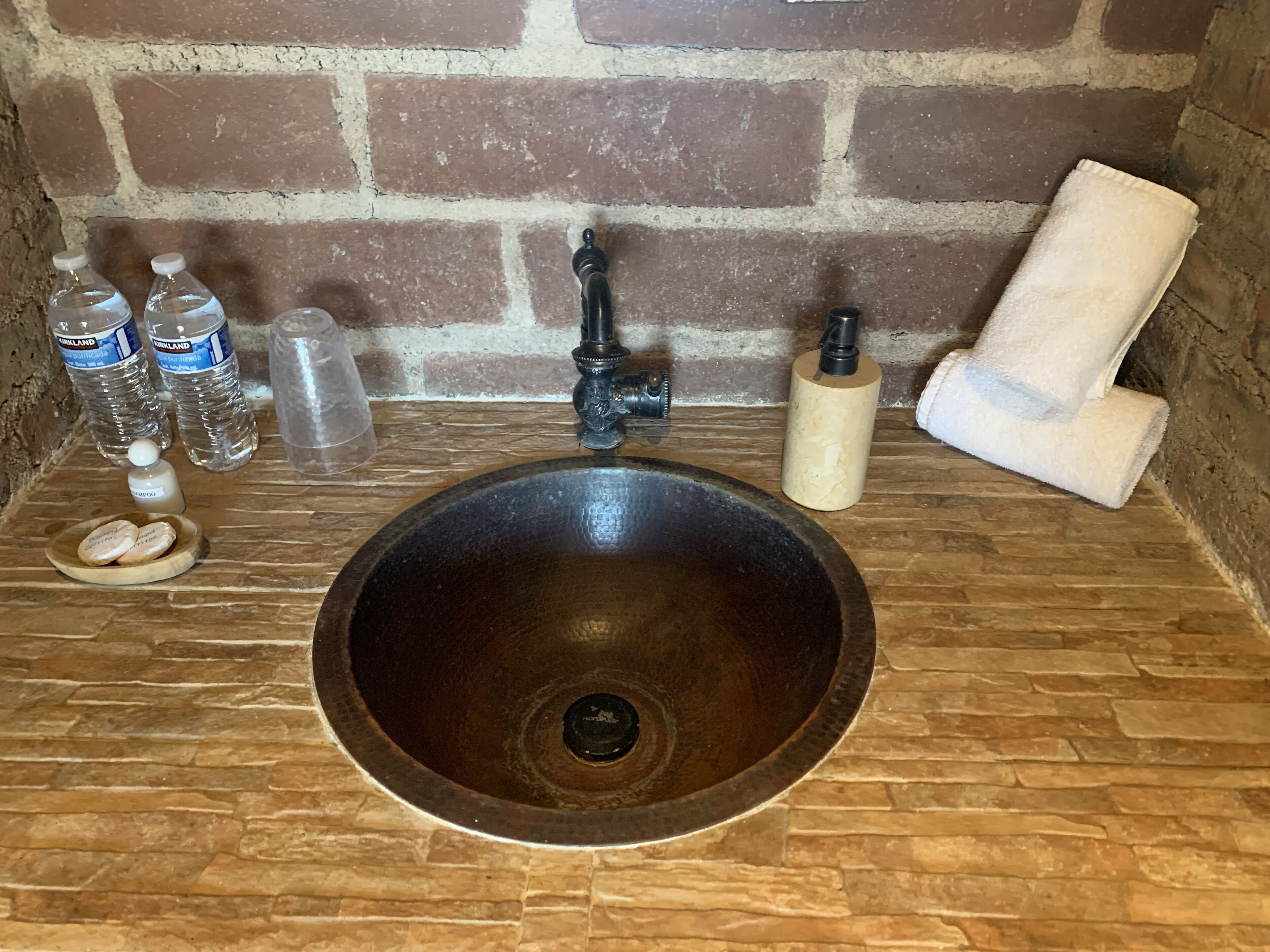 Un lavabo de salle de bain avec un receveur foncé, un robinet et des articles de toilette, notamment du shampoing, du gel douche et une serviette.
