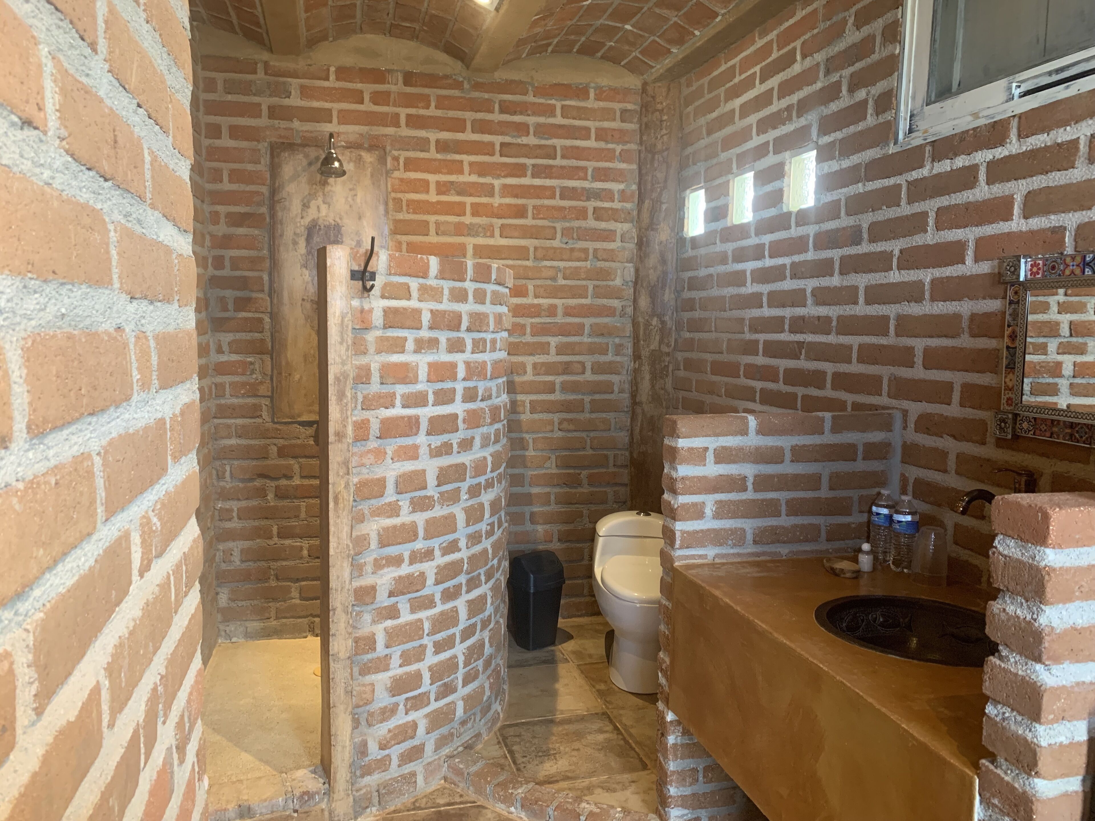 A bathroom with a brick wall, a toilet, a sink, and a shower.