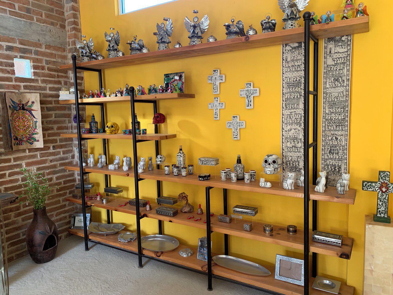 Une pièce avec un mur en briques, un mur jaune orné d’icônes religieuses et des étagères où sont disposés divers objets décoratifs.
