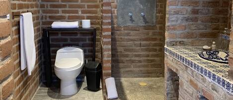 A bathroom with a brick wall, a toilet, a sink with a tiled countertop, and a shower area.