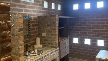 Ein rustikales Badezimmer mit Ziegelwand, Waschbecken mit dekorativer Fliesenrückwand, Holzschrank und Fenster über dem Waschbecken.