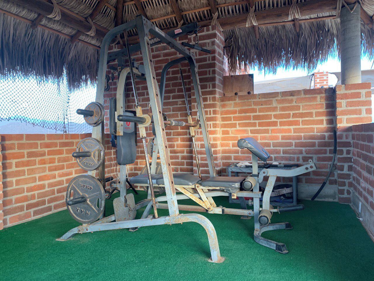 Ett gym med en tegelvägg, ett halmtak och en grön konstgräsmatta.