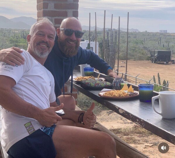 Two people sitting at an outdoor table with food and drinks, overlooking a desert landscape. - Cerritos Baja Eco friendly Boutique stay (El Pescadero)