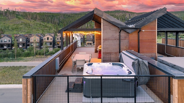 A wooden cabin with a hot tub, deck, and outdoor seating area, surrounded by a forested landscape. - Downtown WP Loft 49 I Rooftop Hot Tub & Lounge I Great Views I Bunk Room I Discounted Attractions (Winter Park)